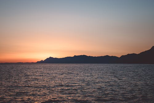 Free Silhouette of a Mountain near a Body of Water at Sunset Stock Photo