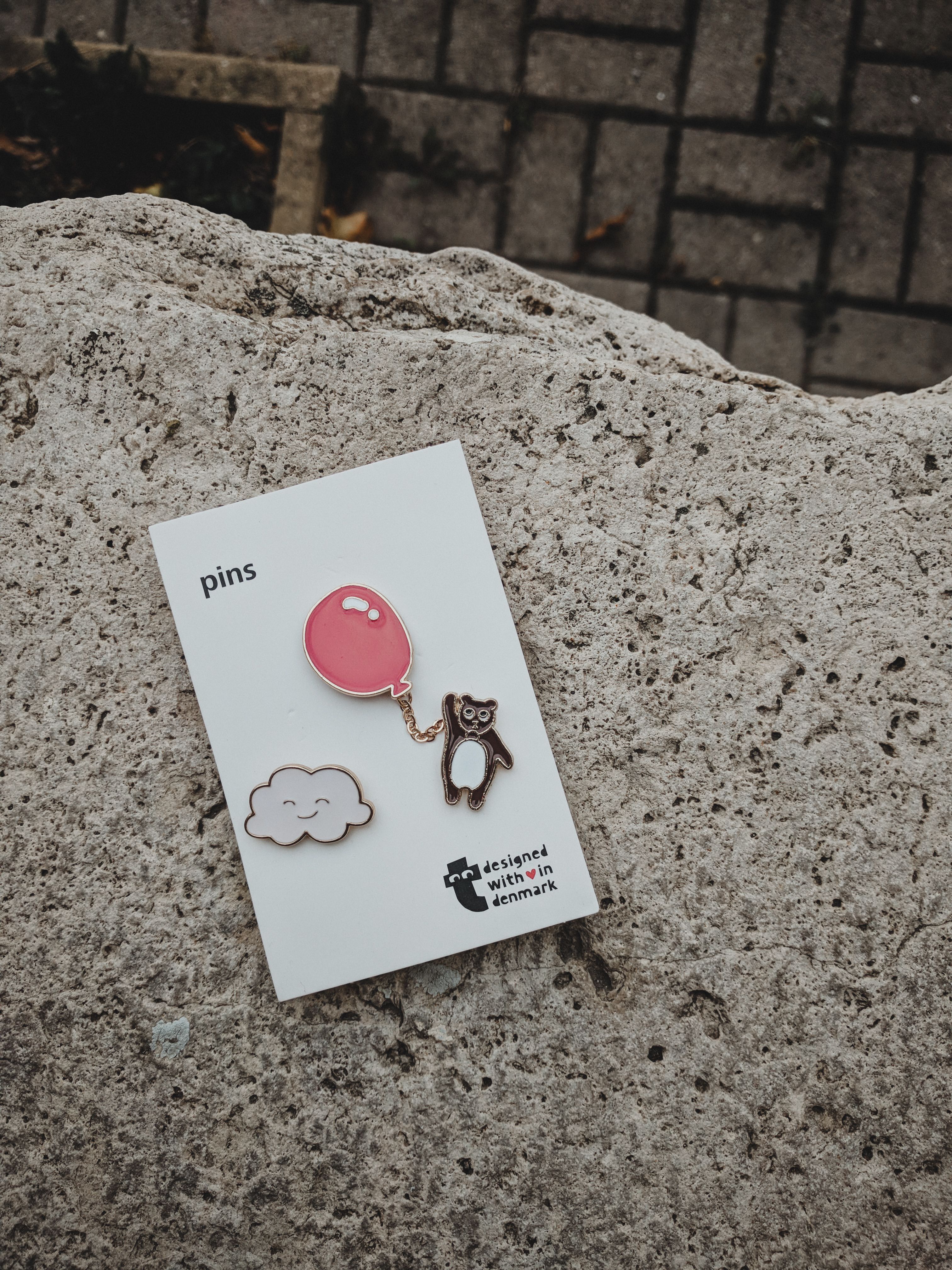 Charming enamel pins featuring a balloon and bear on a stone background, perfect for accessories lovers.