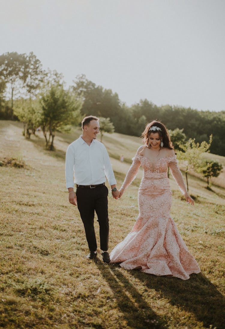 Man And Woman Holding Hands While Walking On Green Grass Field