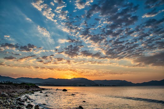 Dramatic sunrise over the ocean with a scenic view of clouds and mountains.