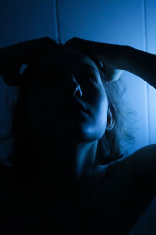 Free Silhouette of a woman with dramatic blue lighting creating a moody atmosphere. Stock Photo