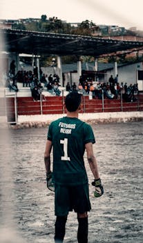 A goalkeeper in a green jersey stands ready on a rustic soccer field in Caldas, Colombia.