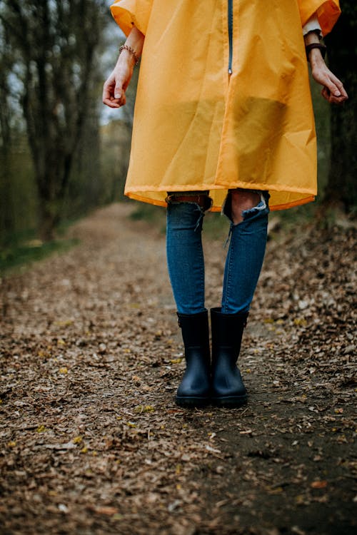 Free Person in Yellow Coat and Black Rain Boots Walking on Dirt Road Stock Photo
