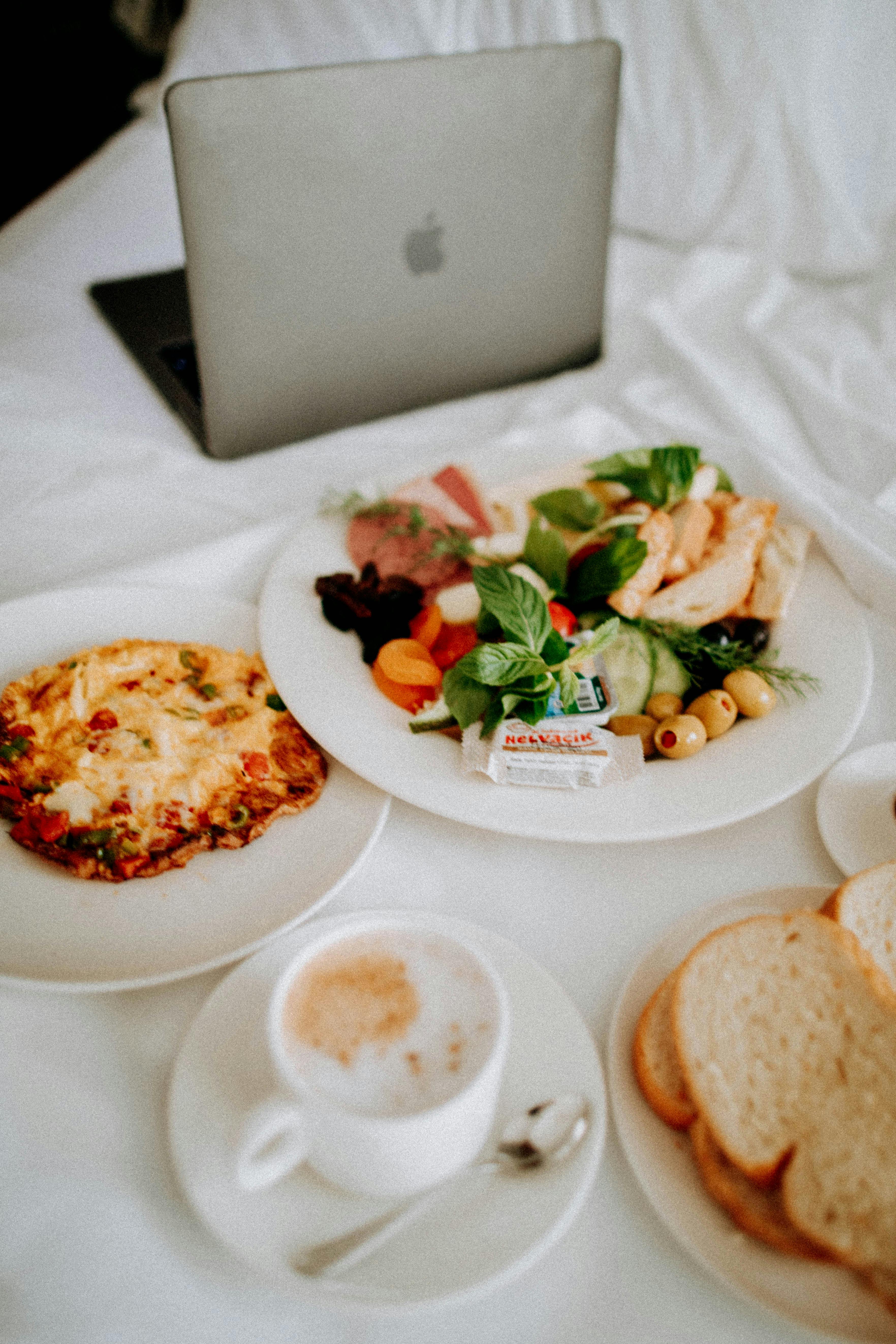 Enjoy a luxurious breakfast in bed with coffee and fresh food beside a laptop.