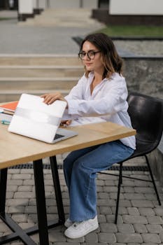 A young woman sitting outdoors, engaging in online learning with a laptop at a table.