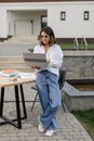 Woman in White Long Sleeve Shirt and Blue Denim Jeans Sitting on Chair While Using Macbook