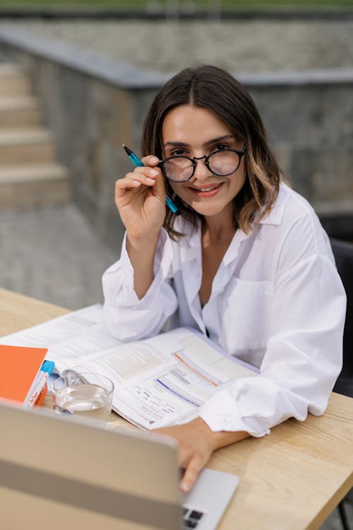 Woman in White Button Up Long Sleeve Shirt Reading While Using Laptop