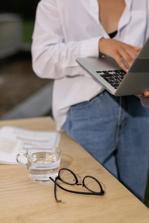 Free Person Holding a Laptop Beside the Wooden Table Stock Photo