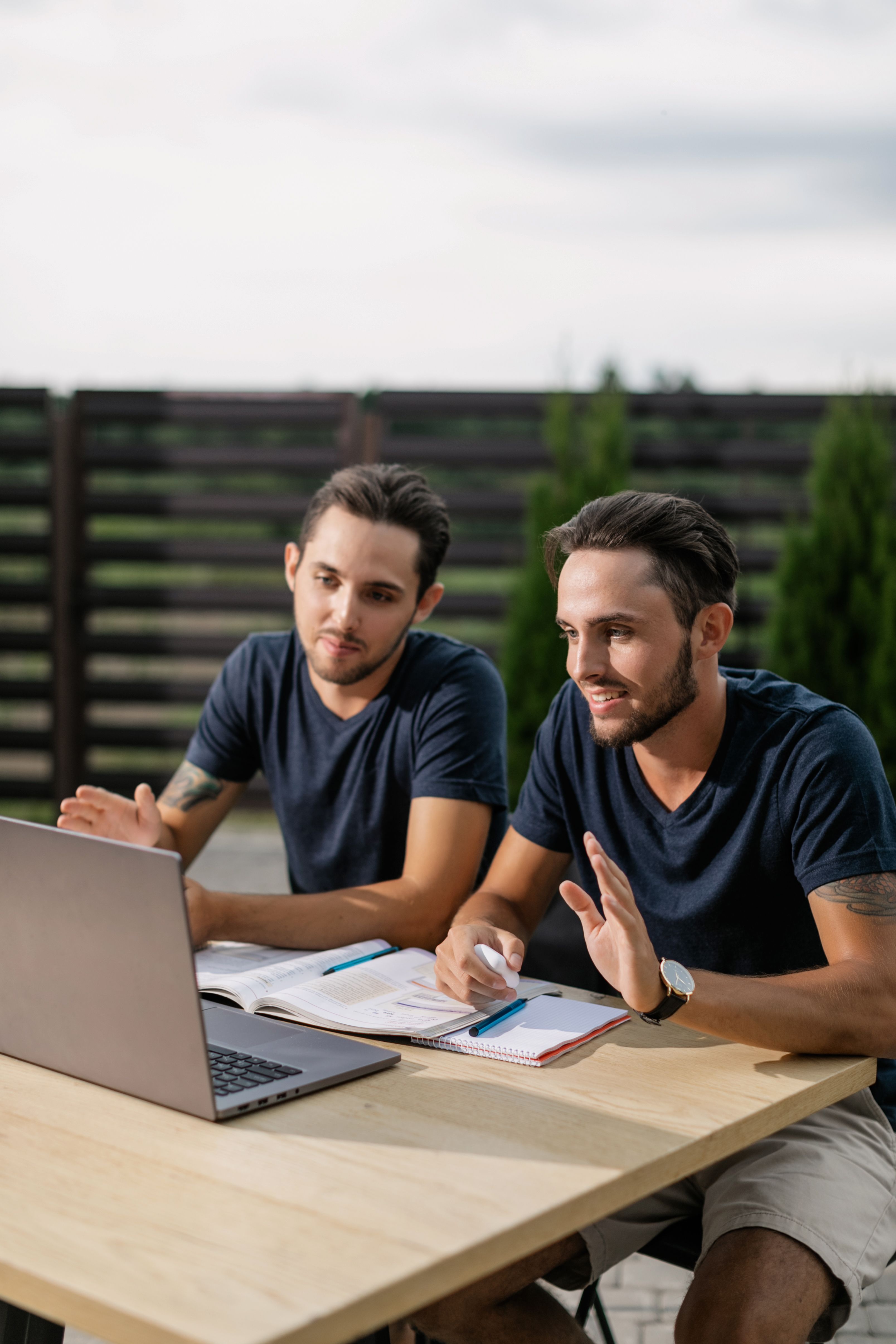 Two twin brothers engaging in online learning outdoors on a laptop.