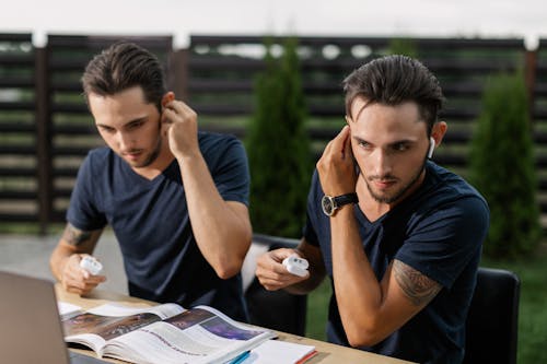 Twins Wearing Earphones Sitting at Table with Magazine

