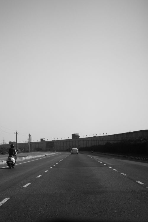 Free Black-and-white image depicting an open highway with a car and motorcycle in motion under a clear sky. Stock Photo