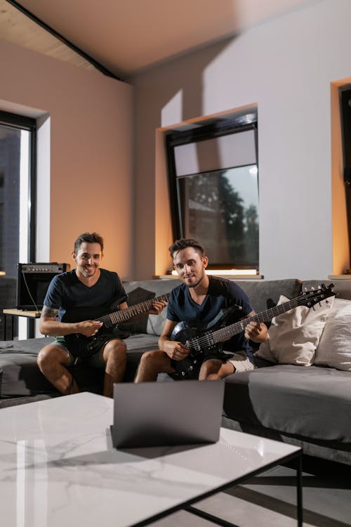 Men Sitting on Gray Sofa Playing Guitars