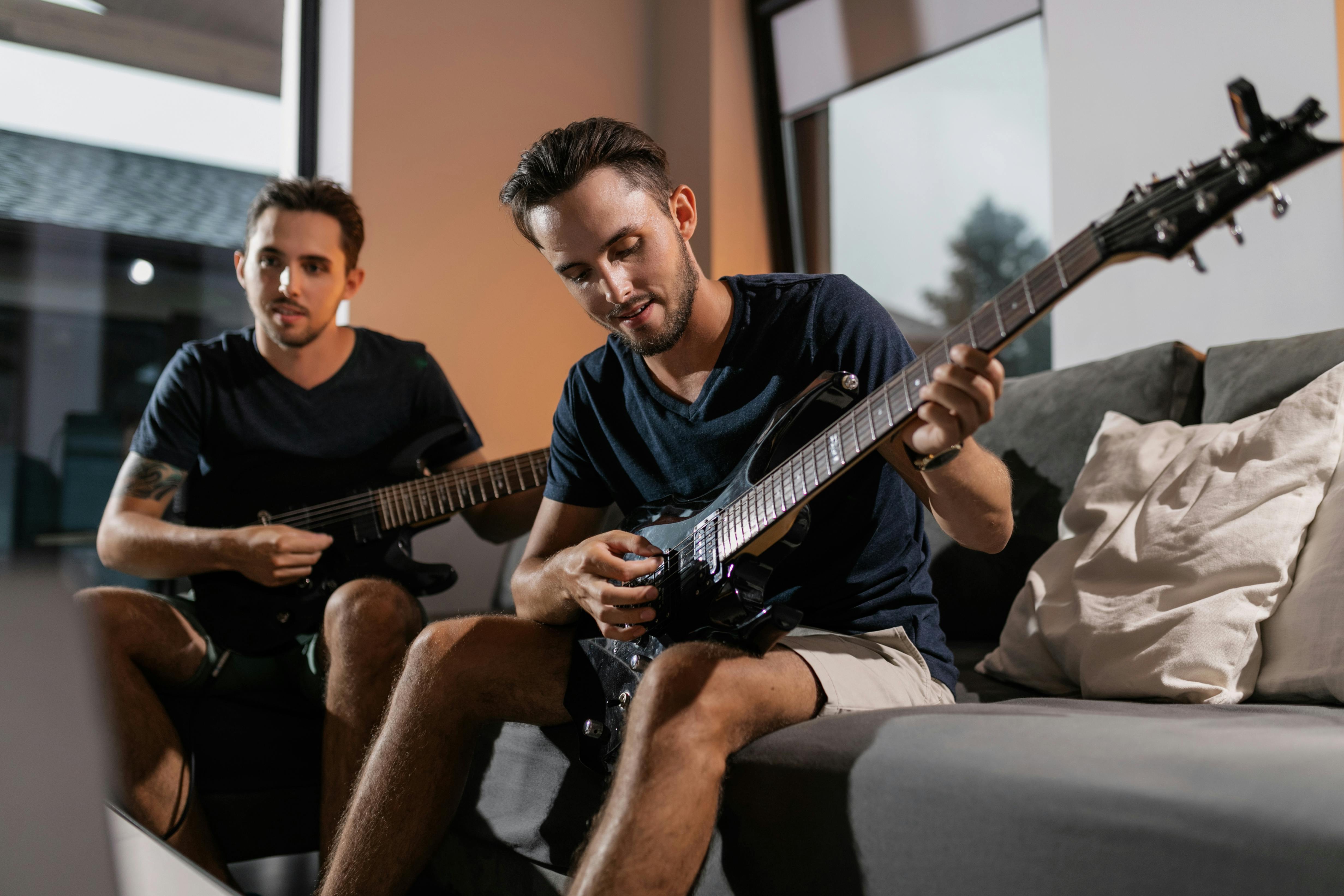 twin brothers sitting on couch while playing electric guitars