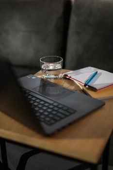 A cozy indoor workspace featuring a laptop, glass of water, and notepad on a wooden table.