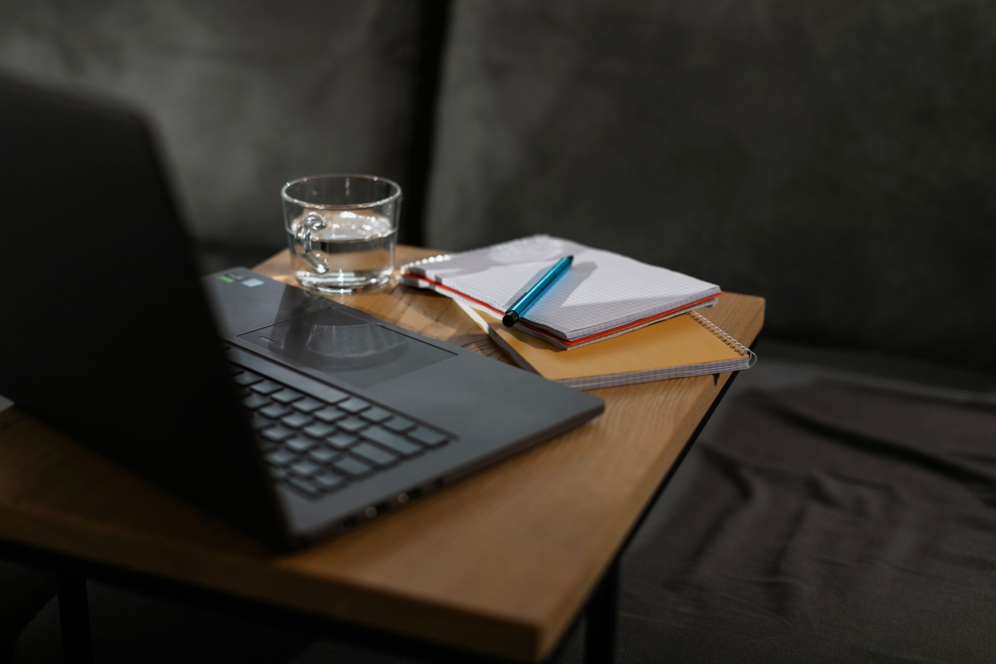 A minimalist workspace featuring a laptop, notebooks, and a glass of water on a wooden table.