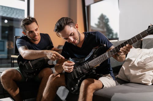 Twin Brothers Sitting on Couch while Playing Electric Guitars