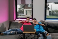 Man in Blue Denim Jeans Sitting on Black Couch Using Macbook