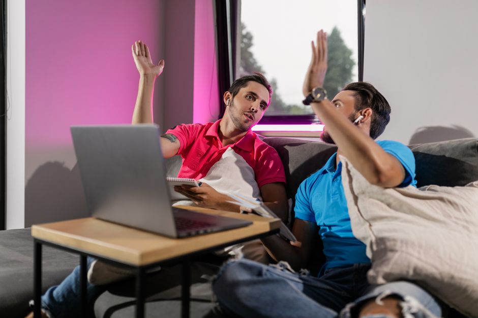 Two men sitting on a couch, engaging in a virtual learning session with laptops. Two men sitting on a couch, engaging in a virtual learning session with laptops.