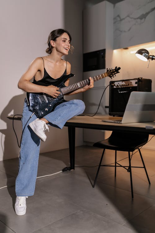 Woman in Black Tank Top and Denim Pants Using an Electric Guitar