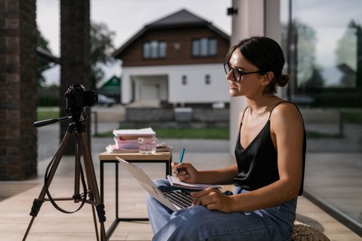 Woman sitting with laptop taking notes for an online class, intense focus outdoors.