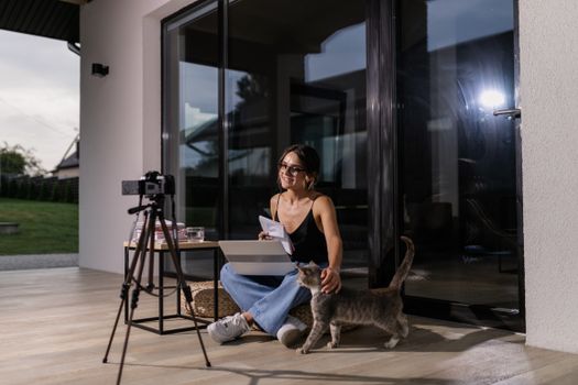 A woman participates in an online class at home, accompanied by her cat, using a laptop.