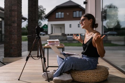 Young woman vlogging outdoors, seated with laptop and camera setup on tripod.