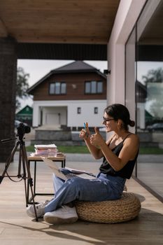 Young woman with eyeglasses posing with camera and laptop, showing thumbs up. Casual summer vibe.