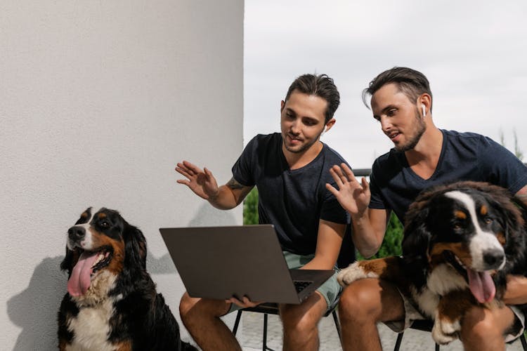 Two Men Sitting While Waving Hello At The Laptop