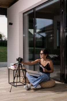 Woman sitting indoors with camera and laptop, engaging in vlogging activity.