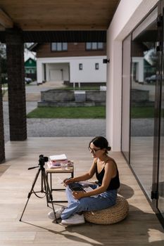 Young woman seated outdoors on cushion using laptop for online class. Modern home learning setup.