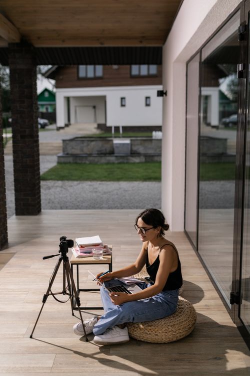 Free Young woman seated outdoors on cushion using laptop for online class. Modern home learning setup. Stock Photo
