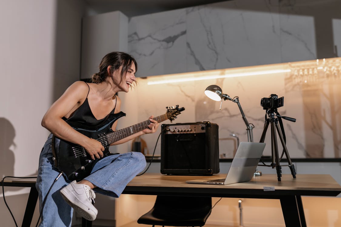 Free Woman in Black Tank Top Using an Electric Guitar In Front of a Laptop Stock Photo