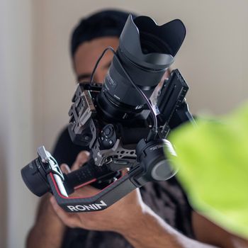 Close-up of a person holding a DSLR camera with stabilizer indoors.