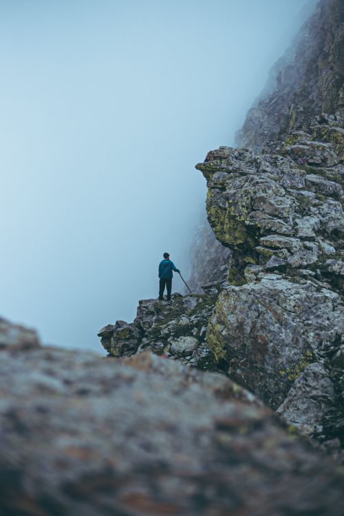 Free A lone hiker stands on a rocky cliff enveloped in fog, capturing the essence of adventure. Stock Photo