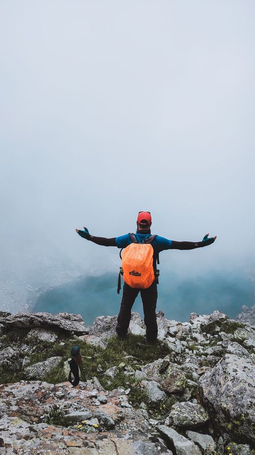 Free Man stands triumphantly on a foggy mountain cliff with arms open, embracing nature's beauty. Stock Photo