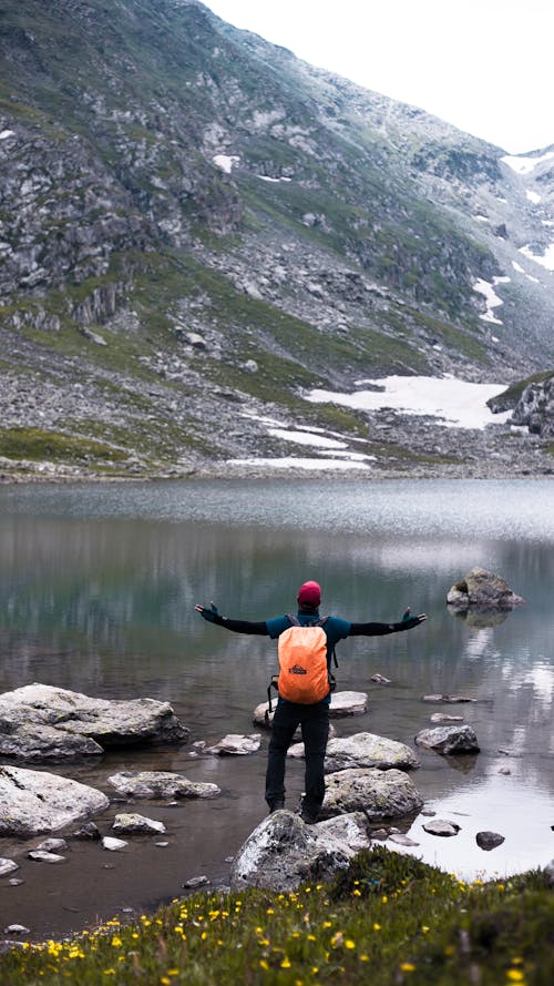 Man in Black Long Sleeve Shirt Standing on Lake near the Mountain