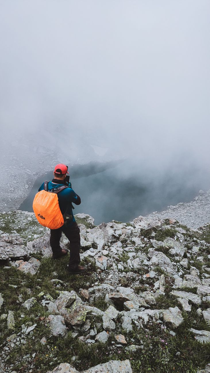 a lone hiker with an orange backpack standing on a high mountain ridge in the Karakoram at sunrise, cinematic vertical outdoor photograph