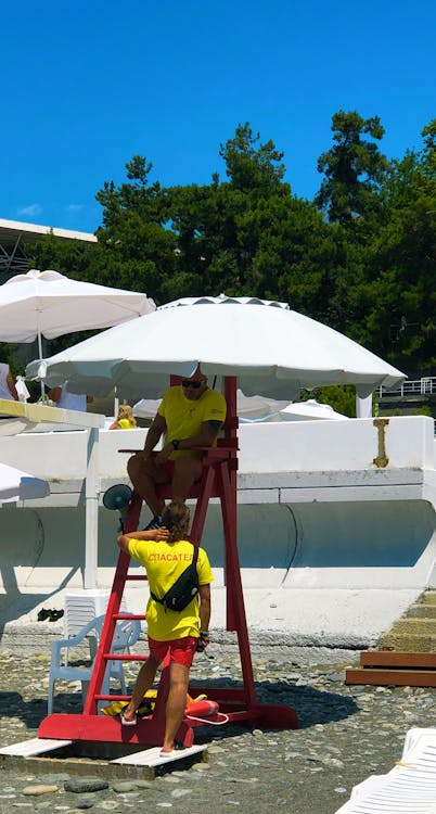 Free Lifeguard Sitting on Wooden Chair Under White Umbrella Stock Photo