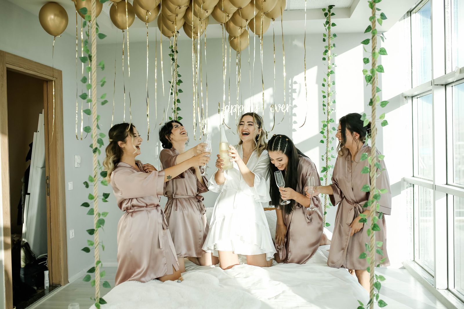 Bridesmaids in matching blush robes celebrate together at a bachelorette party