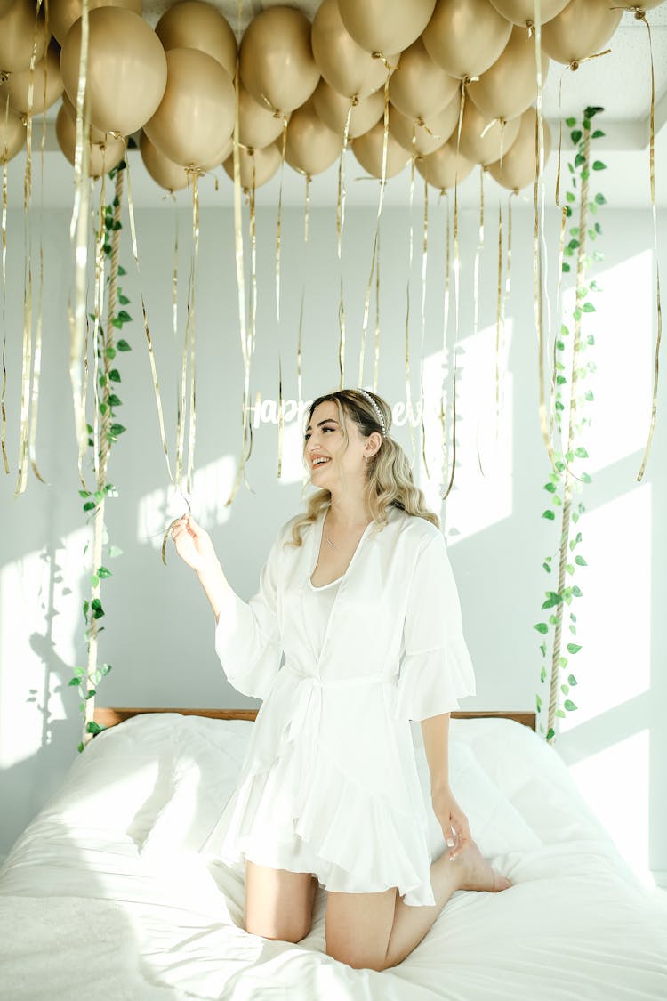 Woman In White Dress On The Bed With Gold Balloons Above 