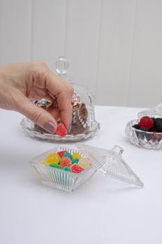 Hand picking gummy candy from a crystal dish, showcasing elegance and color.