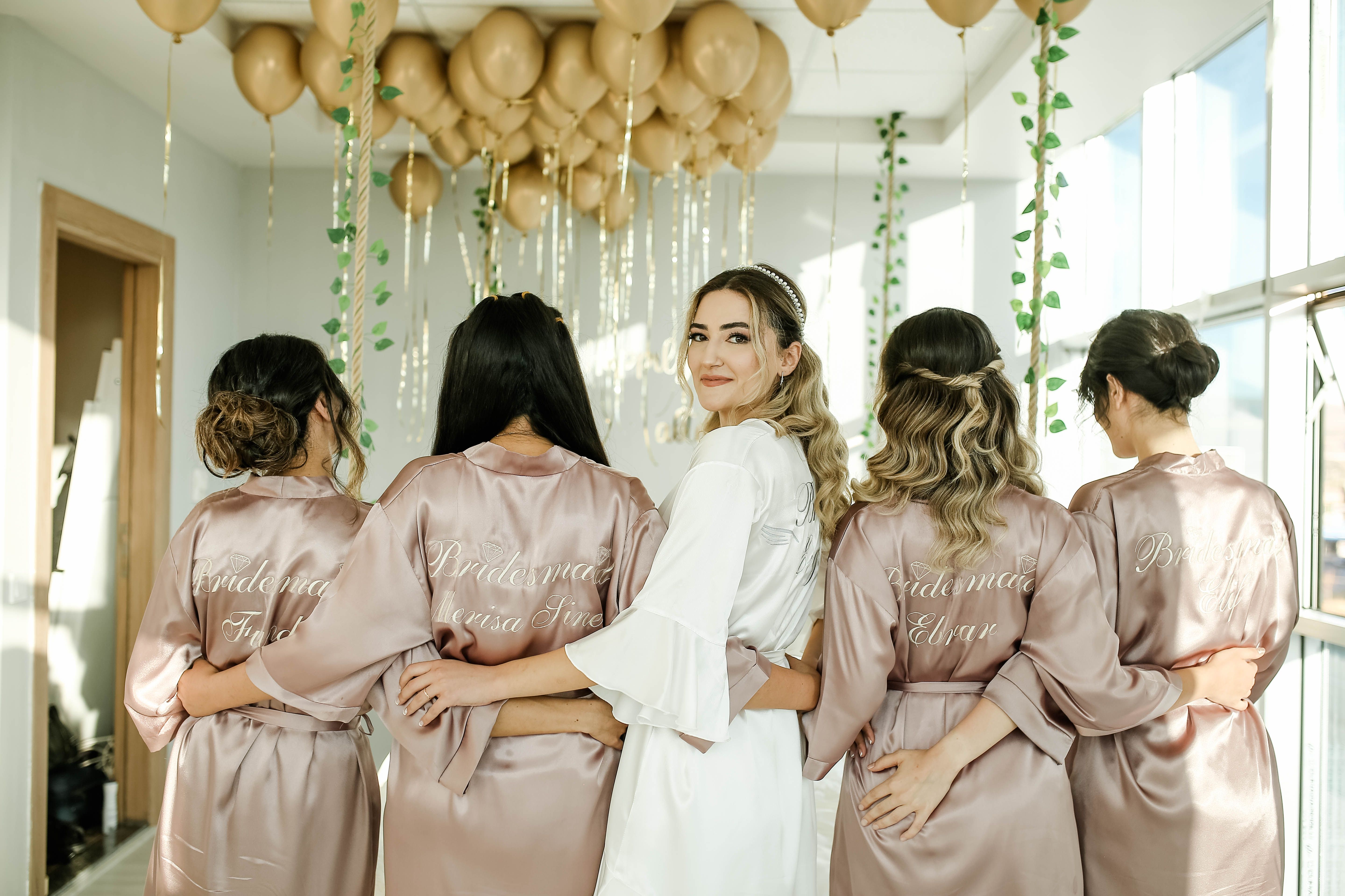 Bride and bridesmaids in matching robes with balloons in a sunny room.