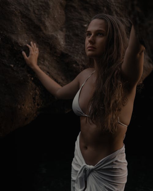 Woman in White Spaghetti Strap Bikini Standing Near the Rock Wall