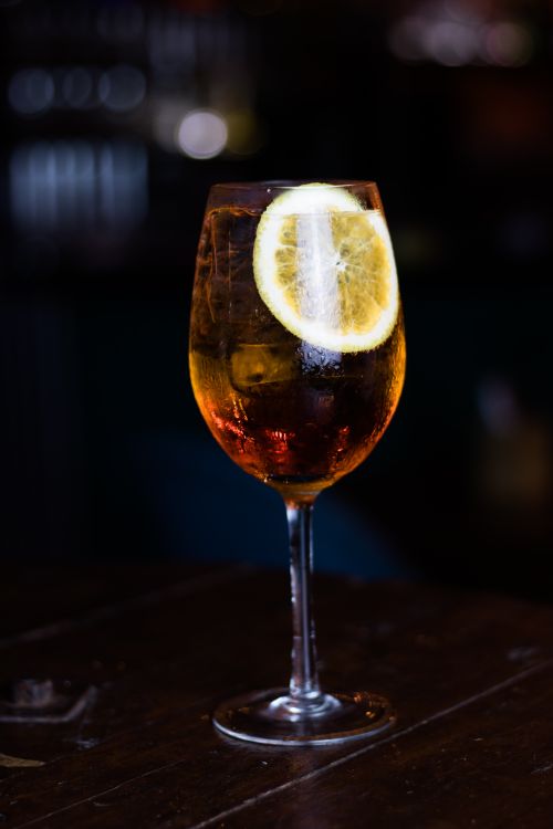 Free Close-up of an Aperol Spritz cocktail with a lemon slice on a rustic table, perfect for nightlife scenes. Stock Photo
