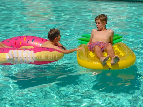 Two boys having fun in a pool with colorful inflatable floaties on a sunny day.