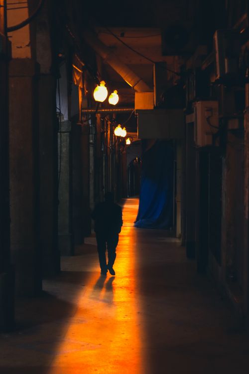 Free A solitary figure walks through a dimly lit corridor casting a dramatic silhouette. Stock Photo