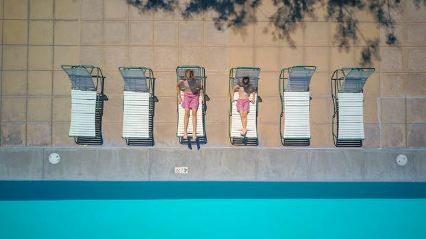 Aerial shot of two boys sunbathing on pool chairs beside a pool, enjoying summertime.