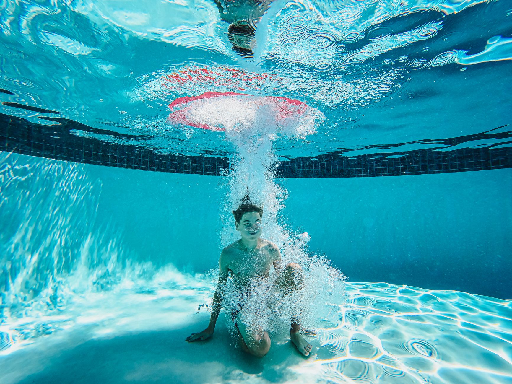 A boy enjoys underwater playtime in a clear swimming pool, surrounded by bubbles.