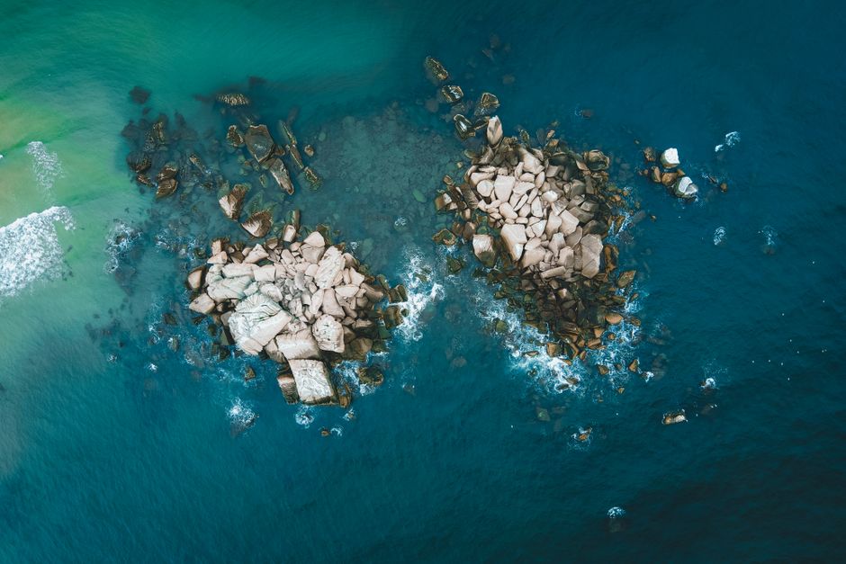 Dramatic aerial shot of rocks in the ocean near Kijal, Malaysia, showcasing vibrant blue waters