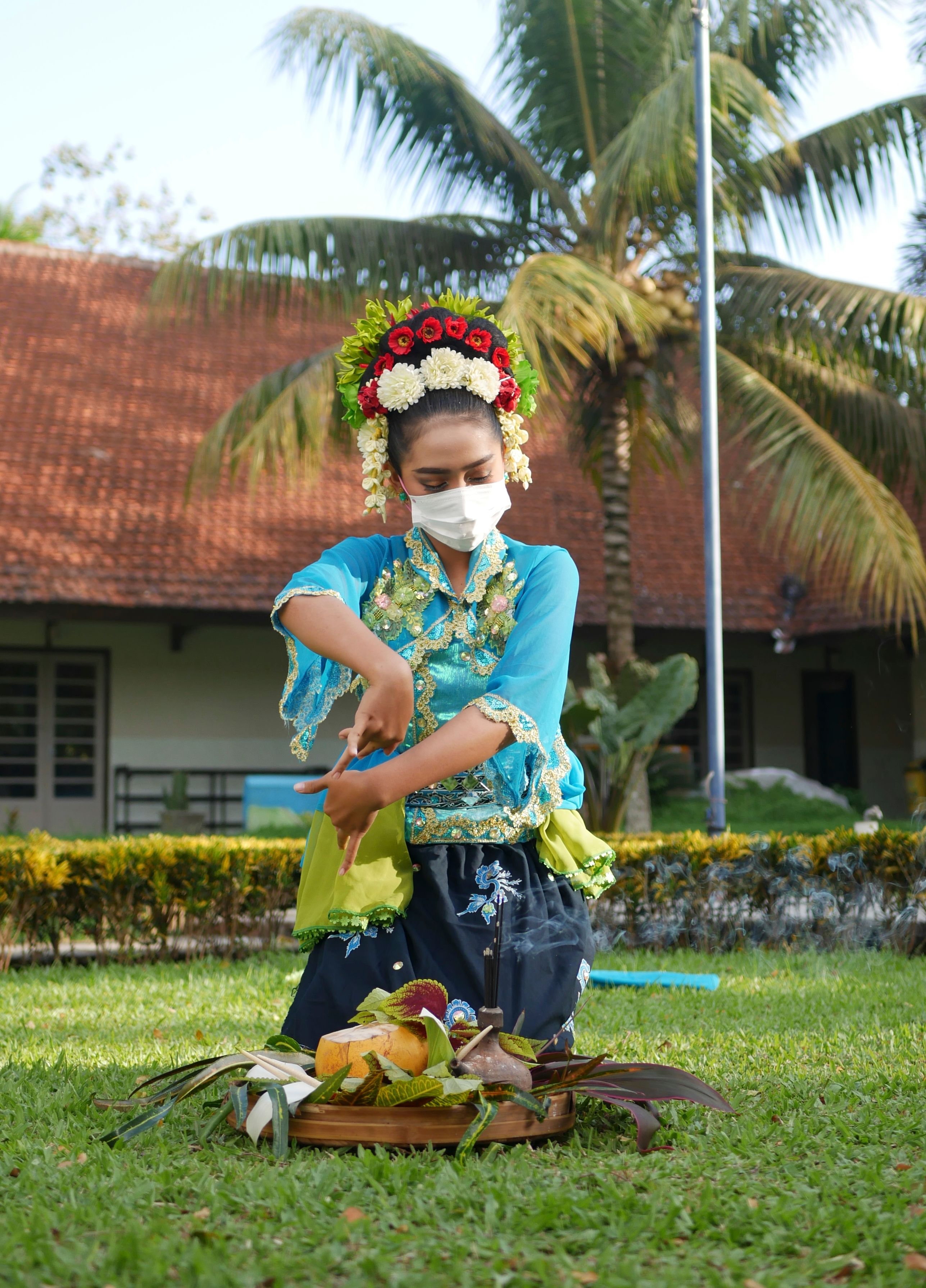 A woman performs a traditional Indonesian dance in a garden, wearing a mask and headpiece.